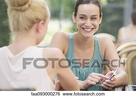 Women chatting outdoors, one woman holding smartphone View Large Photo Image Stock Photograph - Women chatting outdoors, one woman holding smartphone. Fotosearch