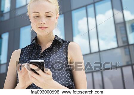 Stock Photograph - Young businesswoman using smartphone outdoors. Fotosearch