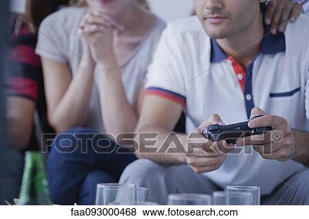 Young man playing video game while friend watches View Large Photo Image Stock Photo - Young man playing video game while friend watches. Fotosearch