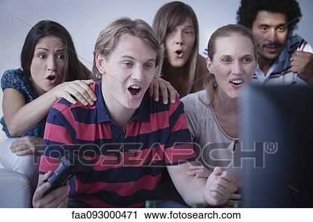Young man playing video games while friends watch with astonishment View Large Photo Image Stock Image - Young man playing video games while friends watch with astonishment. Fotosearch