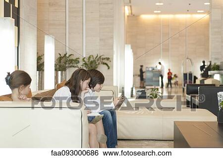Stock Photograph - Young siblings using smartphone in hotel lobby. Fotosearch