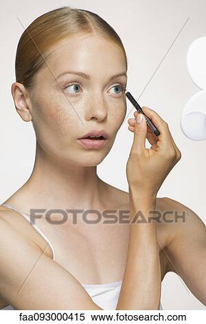 Stock Photography - Young woman applying eyeliner. Fotosearch