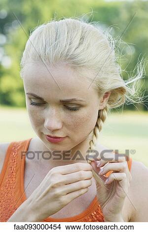 Young woman braiding hair, looking down in thought View Large Photo Image Picture - Young woman braiding hair, looking down in thought. Fotosearch
