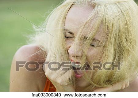 Stock Image - Young woman bursting out laughing with eyes closed. Fotosearch