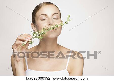 Stock Image - Young woman enjoying frangrence of fresh rosemary. Fotosearch