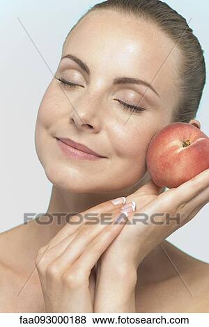 Young woman holding peach to cheek View Large Photo Image Stock Photo - Young woman holding peach to cheek. Fotosearch