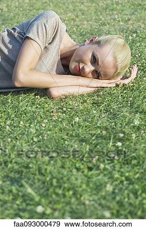 Stock Photo - Young woman lying on grass, portrait. Fotosearch