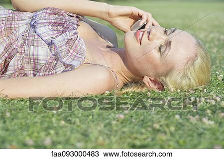 Young woman lying on grass, talking on cell phone View Large Photo Image Stock Image - Young woman lying on grass, talking on cell phone. Fotosearch