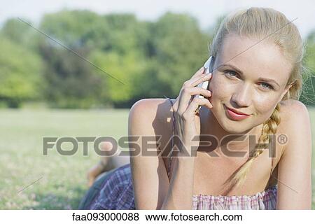 Young woman lying on grass using cell phone, portrait View Large Photo Image Stock Photo - Young woman lying on grass using cell phone, portrait. Fotosearch
