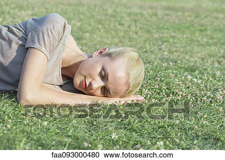 Stock Image - Young woman napping on grass. Fotosearch
