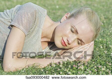Stock Image - Young woman napping on grass. Fotosearch