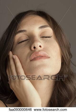 Stock Photograph - Young woman touching cheek and closing eyes, portrait. Fotosearch