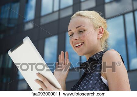 Stock Image - Young woman waving at digital tablet. Fotosearch
