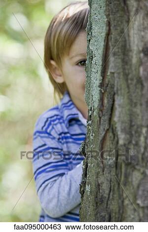Stock Image - Boy peeking from behind tree. Fotosearch