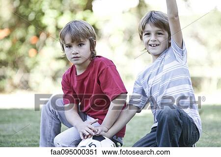 Stock Image - Boys crouching on field with soccer ball, one boy cheering with arm in air. Fotosearch
