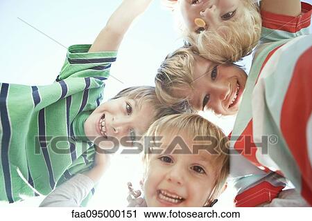 Stock Image - Boys huddling, smiling down at camera. Fotosearch