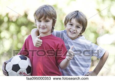 Stock Image - Boys with soccer ball, holding thumbs up, portrait. Fotosearch