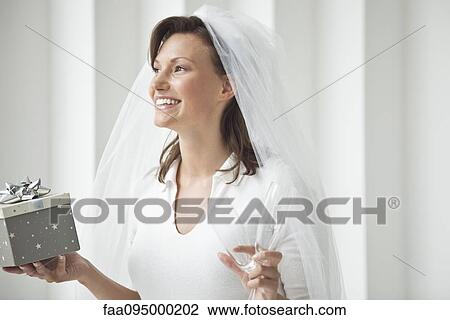 Stock Image - Bride holding champagne flutes and gift box. Fotosearch