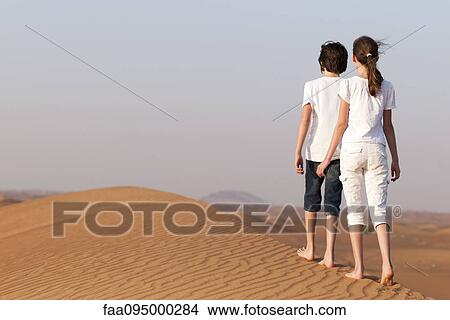 Picture - Brother and sister walking on sand dune, rear view. Fotosearch