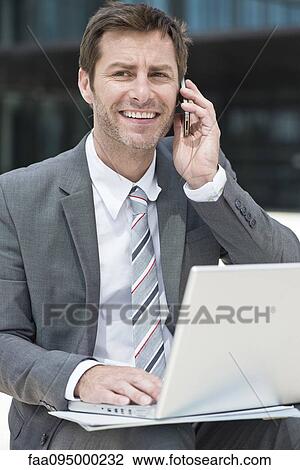 Stock Image - Businessman multitasking while working outdoors. Fotosearch