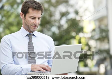 Businessman using laptop outdoors View Large Photo Image Stock Photo - Businessman using laptop outdoors. Fotosearch