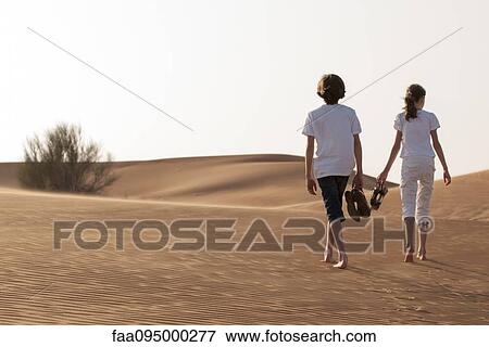 Stock Photo - Children walking in desert, rear view. Fotosearch