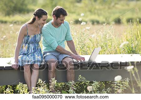 Couple sitting on countryside boardwalk with laptop computer View Large Photo Image Stock Image - Couple sitting on countryside boardwalk with laptop computer. Fotosearch