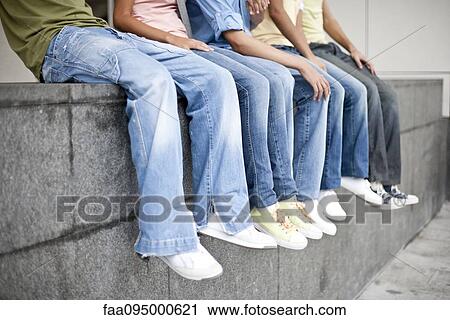 Stock Image - Friends sitting together on low wall, low section. Fotosearch
