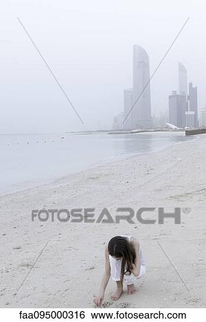 Stock Photograph - Girl looking for seashells at the beach. Fotosearch