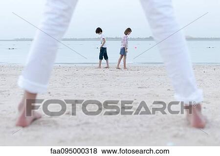 Girl standing on beach, watching siblings at water's edge View Large Photo Image Stock Photo - Girl standing on beach, watching siblings at water's edge. Fotosearch