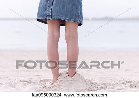 Picture - Girl standing on beach with feet buried in sand, low section. Fotosearch