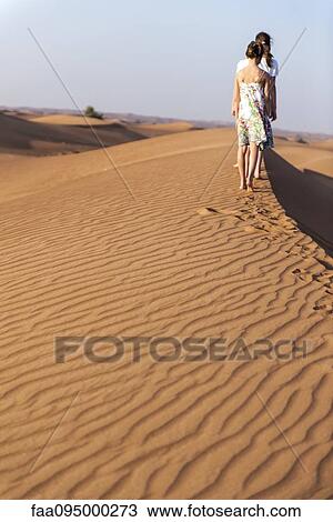 Stock Image - Girls walking on dune, rear view. Fotosearch