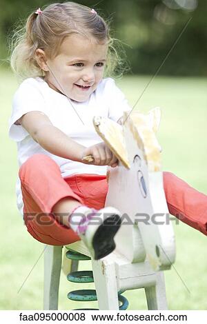 Stock Photo - Little girl riding rocking horse, portrait. Fotosearch