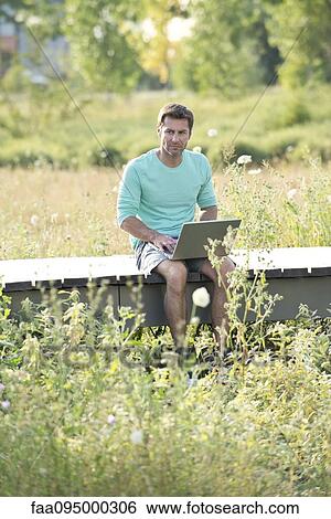 Man using laptop computer while sitting out in countryside View Large Photo Image Stock Photograph - Man using laptop computer while sitting out in countryside. Fotosearch