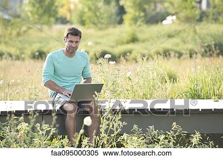 Man using laptop computer while sitting out in nature View Large Photo Image Stock Photography - Man using laptop computer while sitting out in nature. Fotosearch