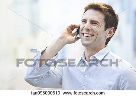 Stock Image - Mid-adult man talking on cell phone, portrait. Fotosearch