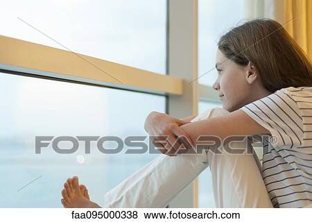 Stock Photo - Preteen girl hugging knees, looking out window. Fotosearch