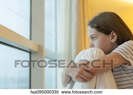 Stock Photography - Preteen girl hugging knees, looking out window. Fotosearch