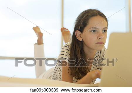 Preteen girl lying on stomach using laptop computer View Large Photo Image Stock Photo - Preteen girl lying on stomach using laptop computer. Fotosearch