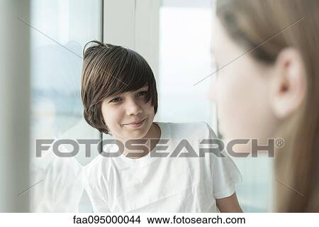 Teenage boy leaning against window, smiling at girl in foreground View Large Photo Image Picture - Teenage boy leaning against window, smiling at girl in foreground. Fotosearch