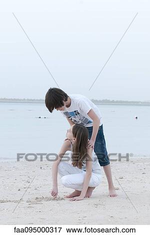 Teenage boy looking over sister's shoulder as she digs in sand at the beach View Large Photo Image Stock Photo - Teenage boy looking over sister's shoulder as she digs in sand at the beach. Fotosearch
