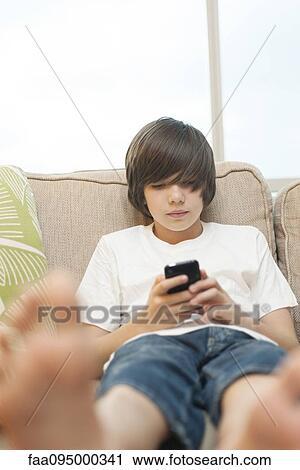 Teenage boy sitting on sofa, using smartphone View Large Photo Image Stock Image - Teenage boy sitting on sofa, using smartphone. Fotosearch