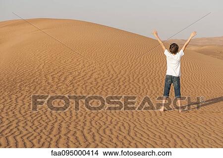 Teenage boy standing in desert with arms raised, rear view View Large Photo Image Picture - Teenage boy standing in desert with arms raised, rear view. Fotosearch