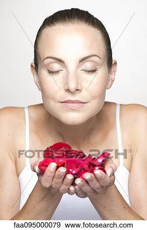Stock Photo - Woman holding rose petals in cupped hands, portrait. Fotosearch