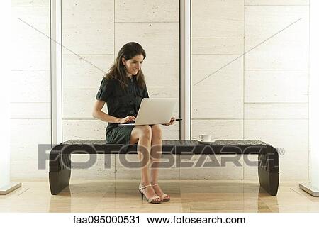 Stock Image - Woman using laptop computer in lobby. Fotosearch