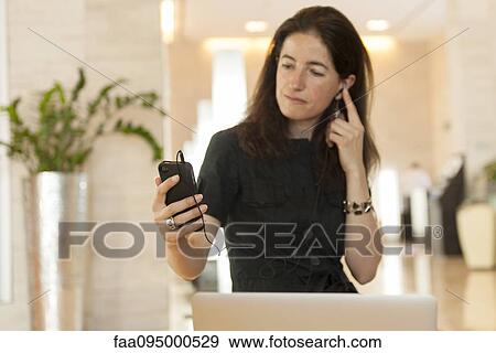 Stock Photo - Woman using smartphone and earphones in lobby. Fotosearch