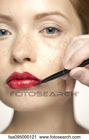 Stock Image - Young woman applying lip color, close-up. Fotosearch
