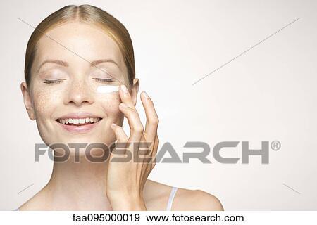 Stock Photo - Young woman applying mositurizer under eye. Fotosearch