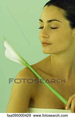 Stock Photo - Young woman holding calla lily, eyes closed. Fotosearch