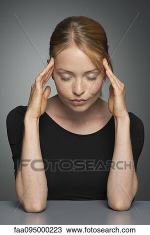Stock Image - Young woman holding head, eyes closed. Fotosearch